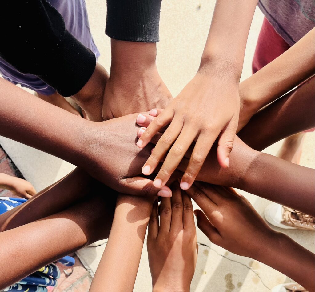 A diverse group of people standing in a circle, stacking their hands together in the center to show unity and teamwork.