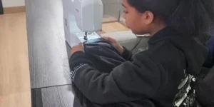 Young person sewing black fabric on a white sewing machine
