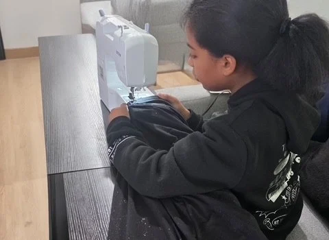 Young person sewing black fabric on a white sewing machine